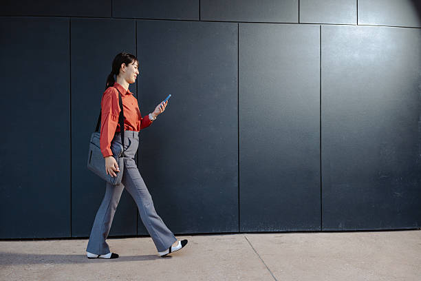 istock Woman walking while focused on smartphone against a modern dark background 2225676445