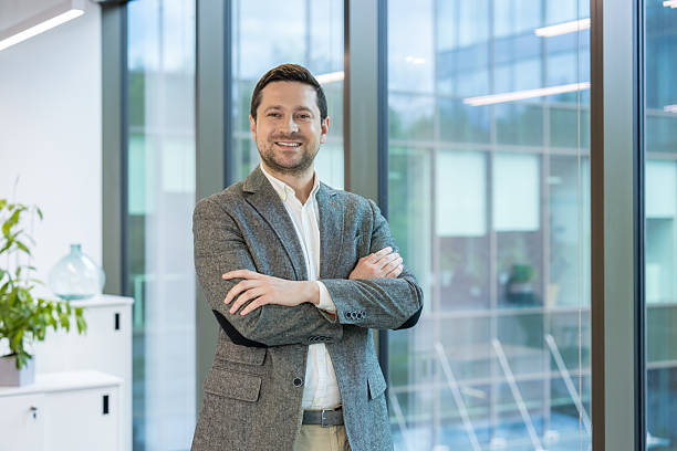 istock A smiling businessman in a blazer standing by a window, looking confident. 2225686470