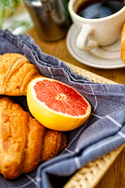 While one buttery croissant sits atop a cup of coffee on a ceramic saucer, creating a cozy and vibrant breakfast atmosphere with warm tones and rustic charm.