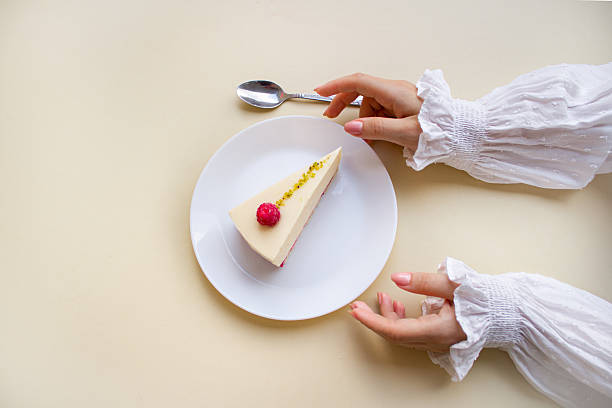 Elegant Woman’s Hands Reaching for a Raspberry Mousse Cake on a White Plate.