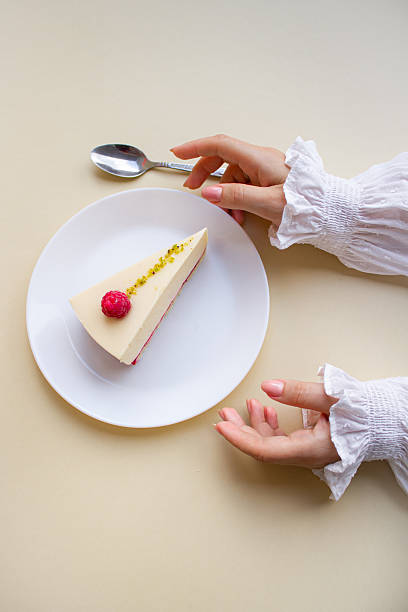 Elegant Woman’s Hands Reaching for a Raspberry Mousse Cake on a White Plate.
