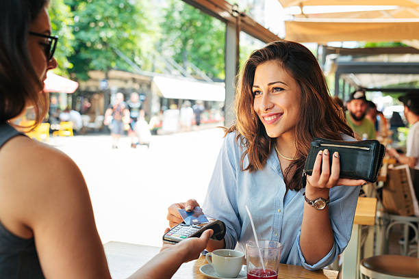 Smiling latino woman is making contactless payment in outdoor summer cafeteria.