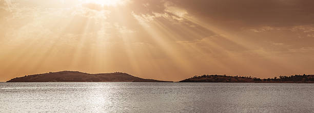 istock Golden sun rays streaming through fluffy clouds, illuminating a calm sea and distant islands during a breathtaking sunset 2225691581