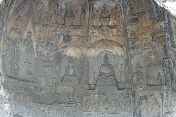 This photograph shows a narrative relief carving, or frieze, from a grotto at Longmen. It depicts a scene with multiple figures in various poses, likely illustrating a Jataka tale (a story of the Buddha's past lives) or a scene of worship. Although heavily eroded, the outlines of the figures and the composition remain visible, offering a glimpse into the storytelling function of grotto art. These narrative panels were educational, teaching Buddhist legends and principles to the faithful.