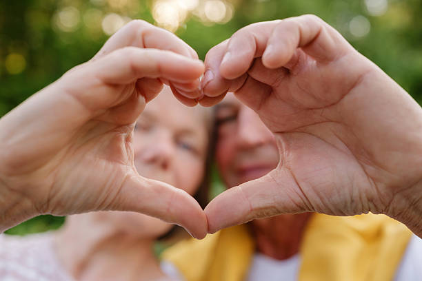 istock A blurred senior couple is in the background while their hands form a heart shape in sharp focus in the foreground, symbolizing love and connection. 2225700551