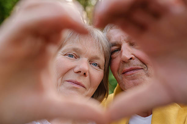 istock A senior couple is framed by hands forming a heart shape in the foreground, looking directly at the camera with warm smiles, expressing enduring love. 2225700578