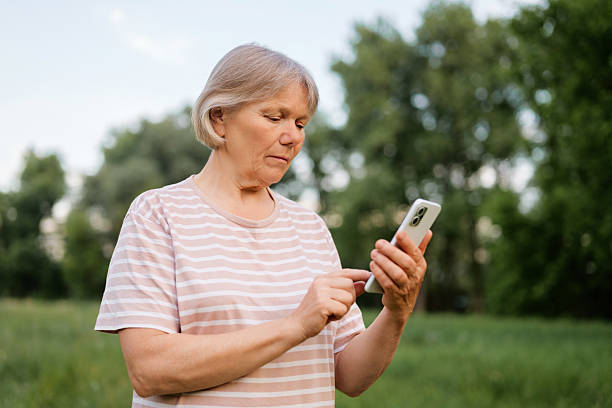 istock A focused senior woman stands outdoors, actively using a smartphone with a concentrated expression against a blurred green background. 2225700601