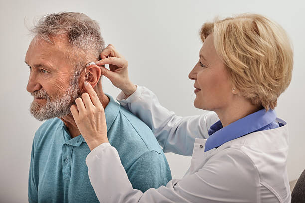 istock Experienced female doctor fitting Behind-The-Ear hearing aid on senior patient's ear while consultation in audiology clinic 2225701232
