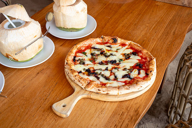 Freshly baked pizza with melted cheese, tomato sauce, olives, and capers on a wooden board. Perfect for Italian cuisine lovers and food photography concepts.