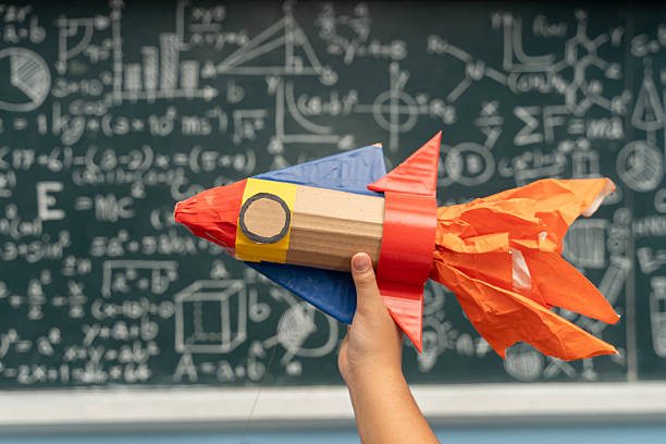 istock Hand holding colorful paper rocket in classroom with chalkboard science education creativity learning concept 2225720175