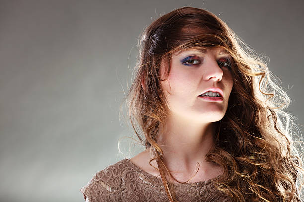 Portrait of mysterious enigmatic woman in studio on grey. Young intriguing attractive girl with long curly hair. Shining light.