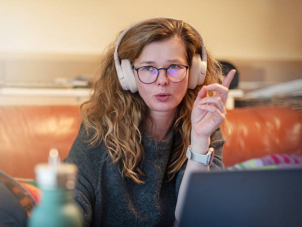 istock Videoconference participant gesturing during call. Middle-aged businesswoman in headphones works from couch at home. 2225726158