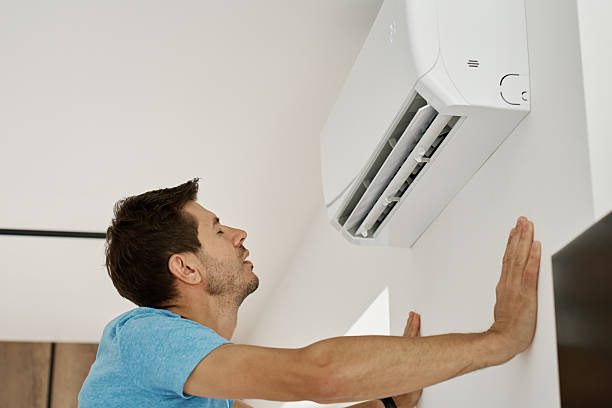 istock Man enjoying cool air from wall mounted air conditioner at home 2225726400