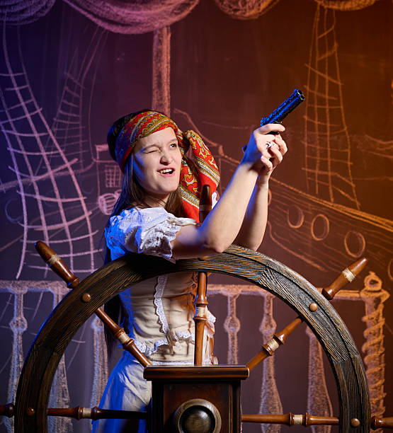 Young pretty woman dressed in pirate costume. She is standing at the helm of the ship. Studio shot, the chalk drawing of a pirate ship floating in the sea on the blackboard as the background