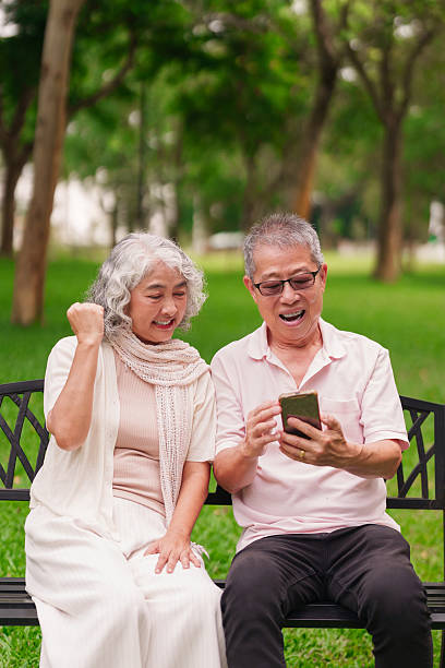 istock Happy Older Asian Couple Using Smartphone on Park Bench Enjoying Retirement Leisure 2225737561