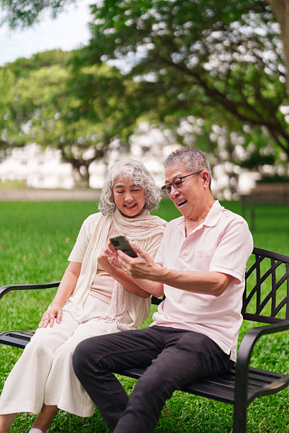 istock Asian Elderly Couple Enjoying Retirement Park Using Mobile Phone Connecting Smiling Laughing Outdoors Technology Leisure Happiness 2225737565