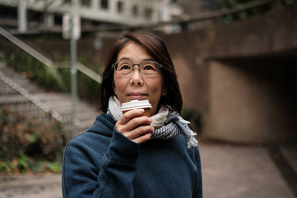 Smiling woman outdoors in worm clothing looking up with a takeaway coffee
