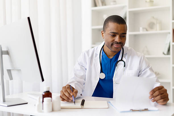 istock Smiling young African American doctor reading document at desk in office 2225750545