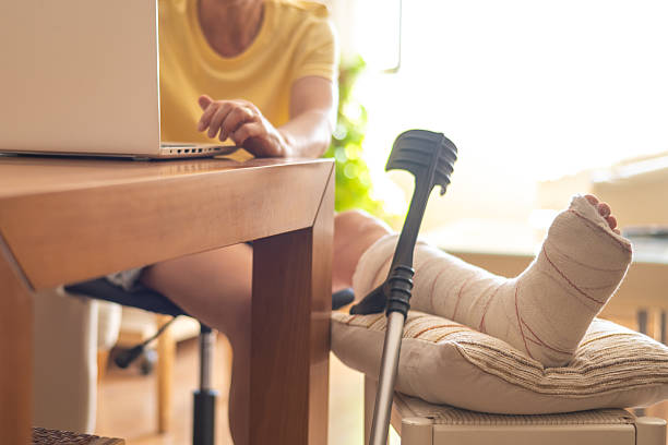 istock Woman with a broken leg and cast works from home, using a laptop while her leg rests on a pillow with crutches nearby, adapting to her physical limitation 2225750554
