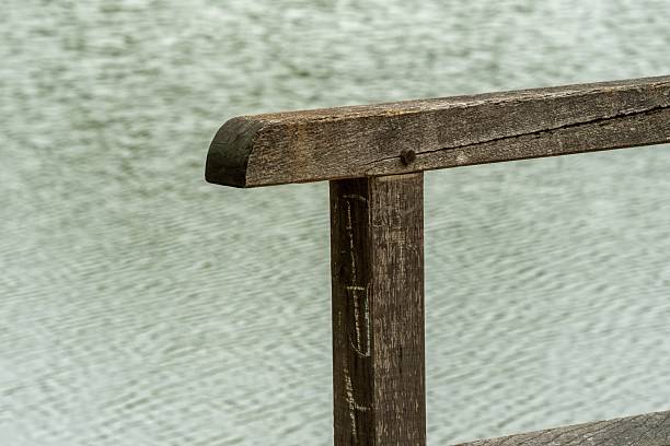 Close-up of weathered wooden railing with blurred water background, evoking tranquility and nostalgia