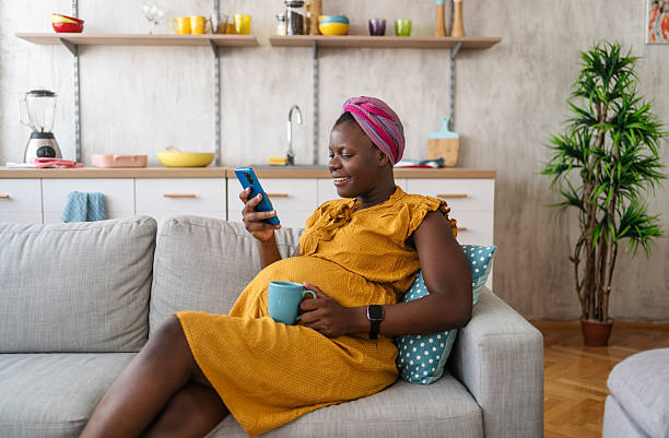 istock Pregnant woman relaxing on sofa using smartphone and drinking tea 2225753158