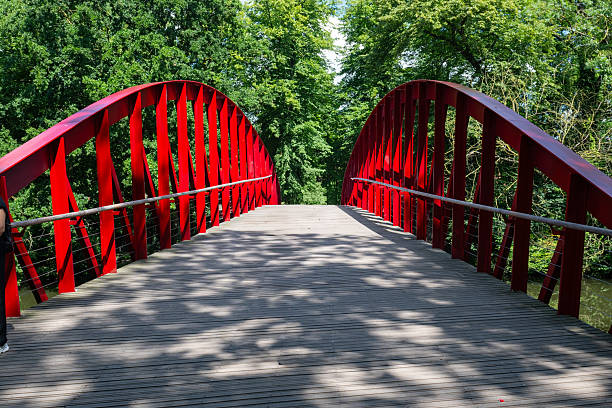 A striking red arched bridge surrounded by lush vegetation, with vertical supports and a wooden walkway.
