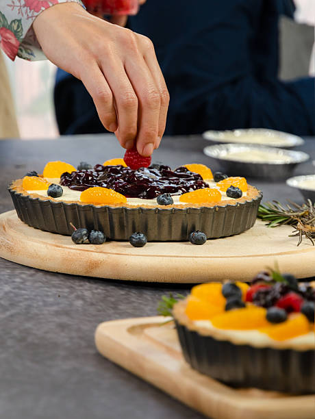 Baker carefully place fresh raspberry on fruit cheese pie of orange and blueberries arranged on creamy filling in fluted pastry tray