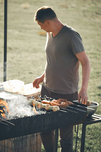 istock Preparing Shish Kebab on a Grill over a Fire with Man Tending Skewers 2225767134