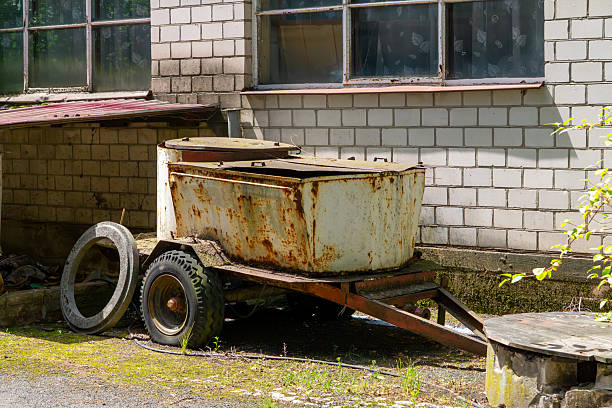 Rusty farm trailer with tank next to brick wall