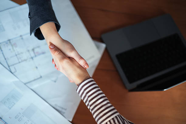 istock Two Professionals Shaking Hands Over Architectural Plans in an Office Setting 2225770304