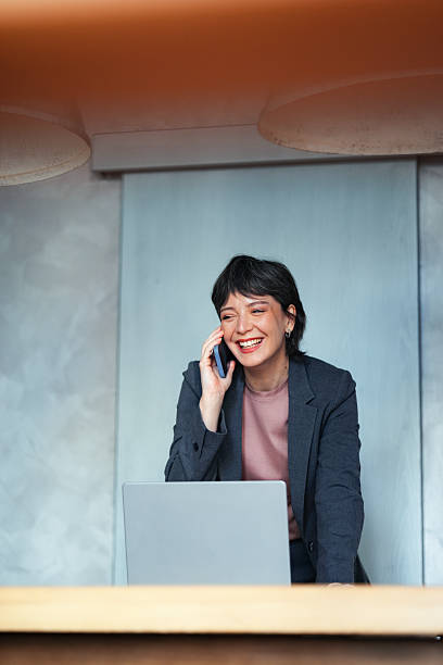 istock Confident Businesswoman Smiling While Working on Laptop and Talking on Smartphone 2225770407