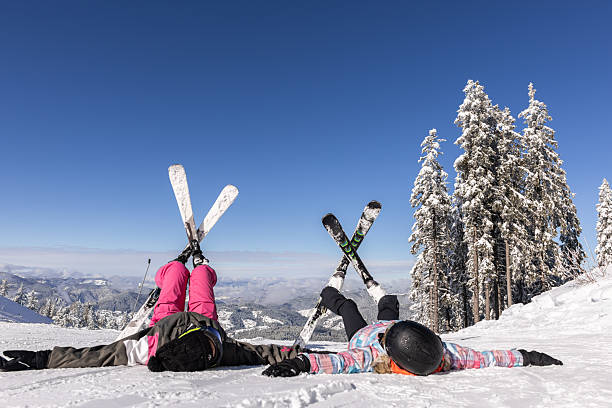 Cheerful female skiers lying on snow and enjoying sun while resting after the descent on slope