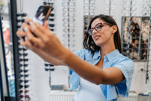 istock Young Woman Taking Selfies Using Phone While Trying On Eyeglasses In An Optical Shop 2225771709