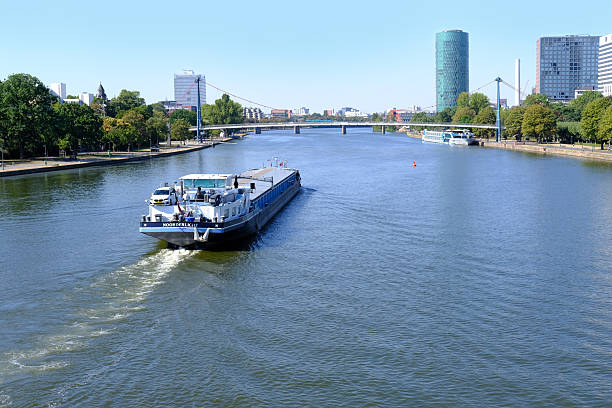 Main River Frankfurt, barges navigating, modern city skyline, bridge, green trees, clear blue sky, urban landscape, European process industry, German manufacturer, Frankfurt - June 14, 2023