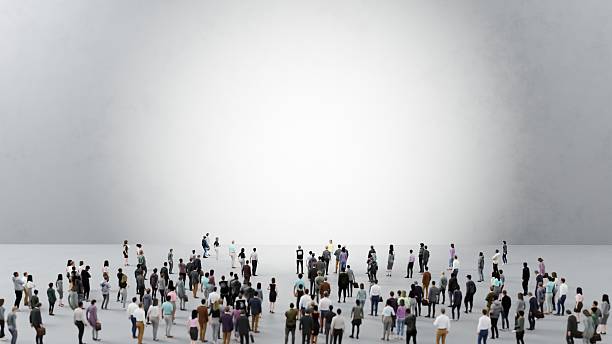 istock Large group of business people standing in a large empty space facing a bright light source 2225781075