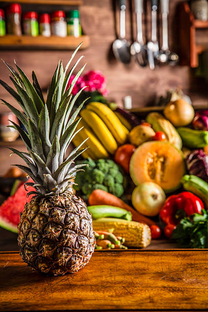 Fruit and vegetable themes: Close-up of Pineapple with organic tropical fruits and vegetables in old fashioned rustic kitchen. Bananas, Watermelon, carrots, bell pepper, pineapple, onions, lettuce, broccoli.