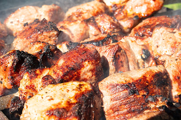 Pieces of pork meat are strung on skewers. The meat is fried at high temperature from the coals in the grill. Close-up.