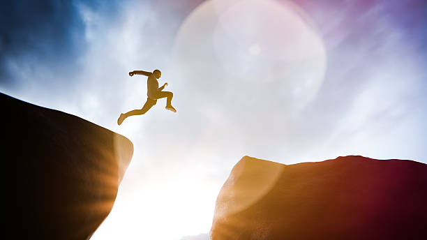 istock Man leaping between two cliffs at sunset, symbolizing courage, determination, and overcoming challenges 2225789393