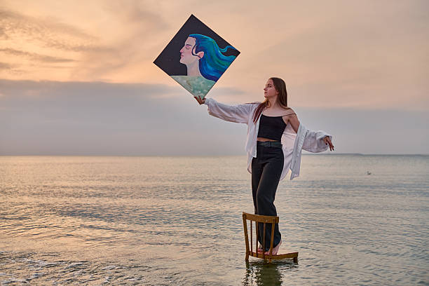 istock Young female painter balances on chair in serene beach setting 2225790008