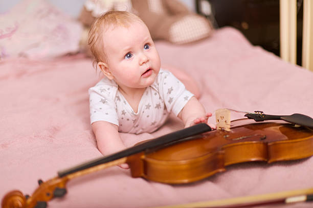 istock Curious baby girl with violin on soft pink bedding 2225790024