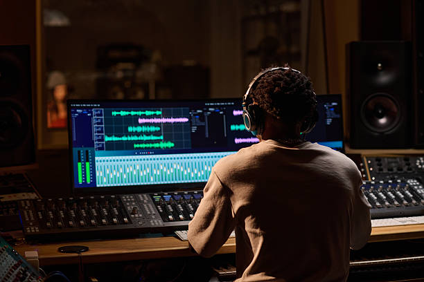 istock Young Adult Black Man Wearing Headphones Editing Audio Waveforms in Studio 2225790113