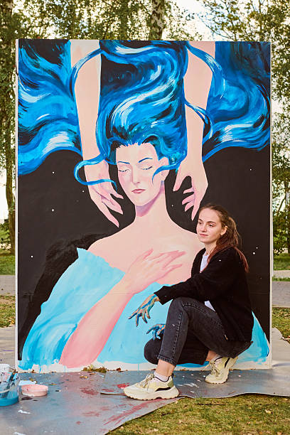 Young female artist creating outdoor mural with blue elements