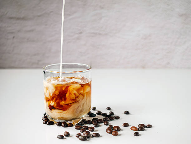 Latte coffee, Milk pouring from a milk jug into a glass of iced coffee with coffee beans on a white background stock photo