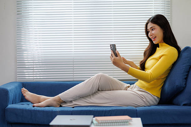 istock Young woman video calling while relaxing on sofa at home 2225794182