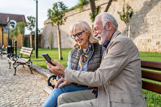 istock Smiling senior couple using smartphone on park bench 2225805883