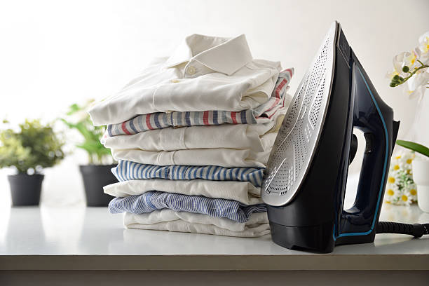 istock Steam iron and stack of folded shirts on white furniture 2225806271