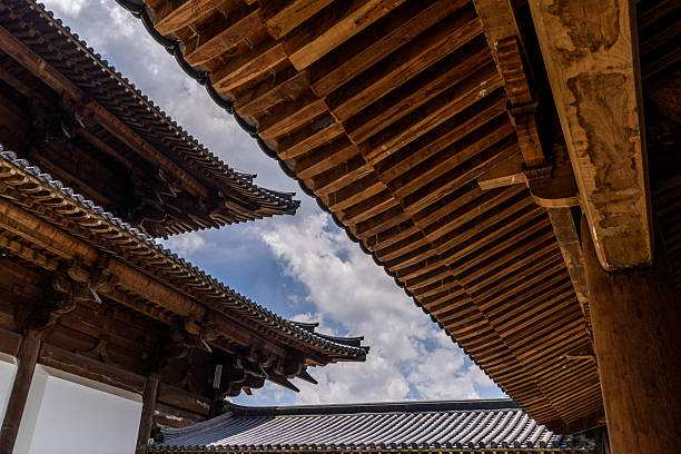 The image isolates a beam tail with carved scrollwork and a plain rafter. Background is soft sky. Use: architectural close-up, traditional carpentry reference, cultural design resource.