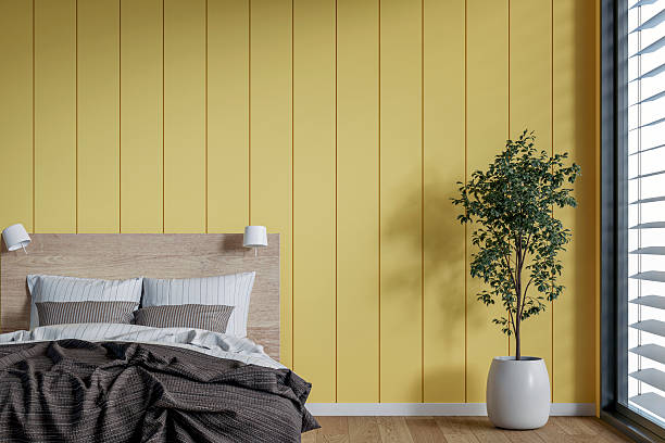 istock Front, close-up view of a modern, minimalistic bedroom with a bed, an empty yellow shiplap paneled wall, a potted plant, windows and decoration 2225815744