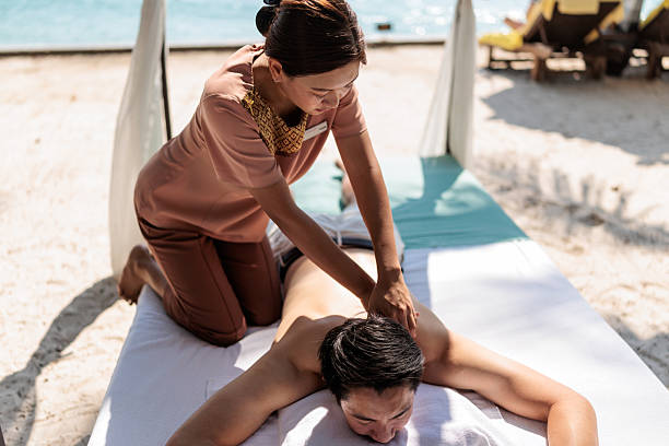 An experienced massage therapist provides a soothing massage to a guest on a comfortable bed set up on a serene tropical beach.