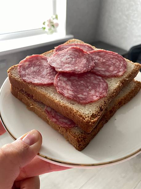sandwich with sausage on a white plate. a sandwich consisting of two slices of bread with several circles of sausage on each. The sausage has a pink tint. The bread is light, slightly coarsely ground